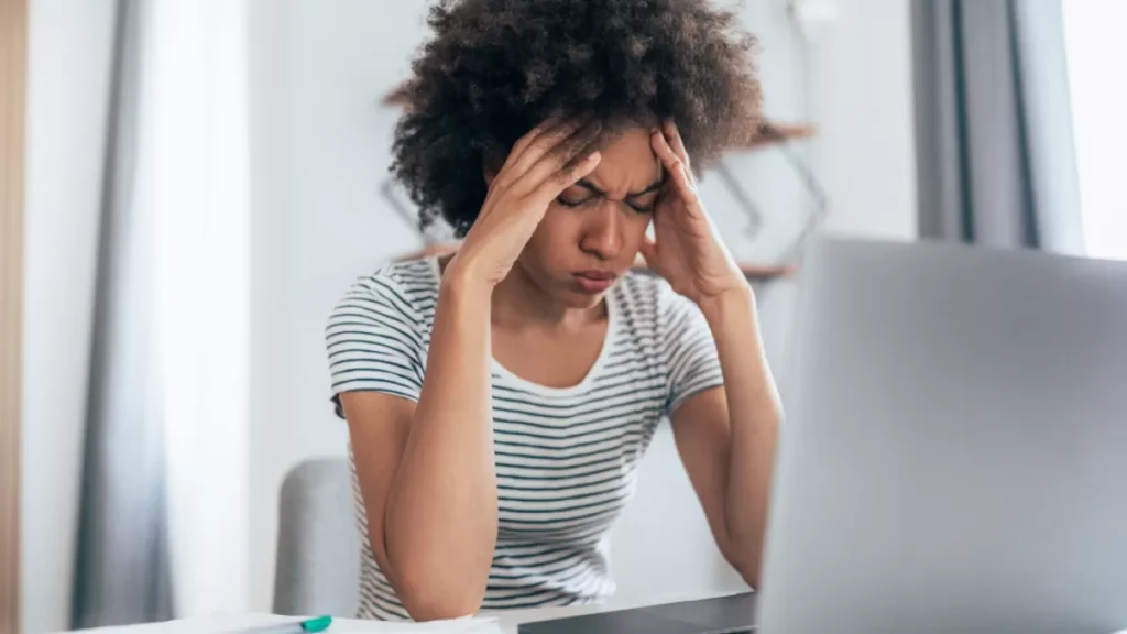 Stressed interpreter at her desk with hands on her temples, exhausted between OPI calls